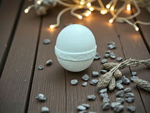 Load image into Gallery viewer, Bath bomb on a wooden surface with decorative lights and stones