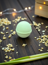 Load image into Gallery viewer, Green bath bomb on a wooden surface with dried flowers and string lights in the background