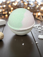 Load image into Gallery viewer, Bath bomb on a wooden surface with blurred lights in the background
