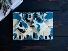 Load image into Gallery viewer, Blue and white swirl handmade soap bars arranged neatly on a dark wooden surface with a white towel and lavender sprigs in the corner