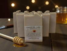 Load image into Gallery viewer, Row of oatmeal, milk, and honey soap bars on a wooden surface with a jar of honey and honey dipper.
