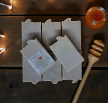 Load image into Gallery viewer, Bar of soap with a label on a wooden surface next to a jar of honey and a honey dipper.