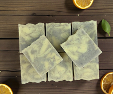 Load image into Gallery viewer, Orange + Patchouli soap bars with orange slices and leaves on a wooden surface