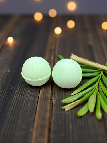 Two green bath bombs on a wooden surface with green leaves and blurred lights in the background