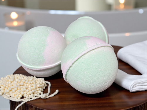 Three green bath bombs on a wooden surface with a towel and beads in the background.