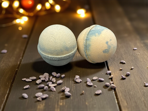 Two bath bombs on a wooden surface with small stones and blurred lights in the background