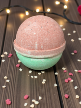 Load image into Gallery viewer, Two-layered bath bomb on a wooden surface with decorative lights in the background
