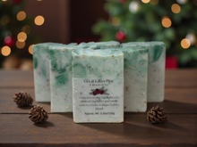 Load image into Gallery viewer, Green soap bars with a label on a wooden surface, Christmas tree in the background
