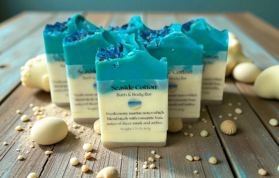 Handmade Seaside Cotton Soap bars with ocean-blue and cream layers, topped with sea salt-like crystals, displayed on a wooden surface with seashells and sand