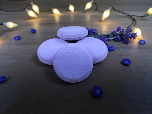 Purple macaron cookies on a dark surface with decorative lights and lavender flowers.